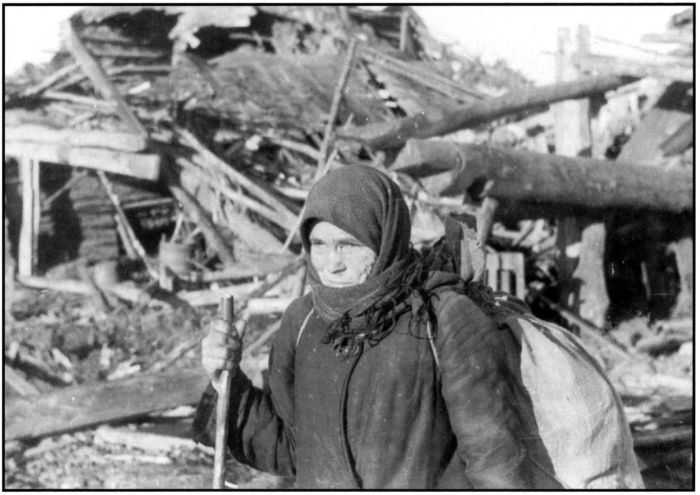 Destruction of the village of Krutiza. Showing an elderly peasant woman carrying her possessions in a sack as she walks past the tumbled down remains of a wooden building. [Gelatin silver photograph. Printed USSR, no. 8788, dated October 1942. Argus Collection, Box 57B] [photograph]