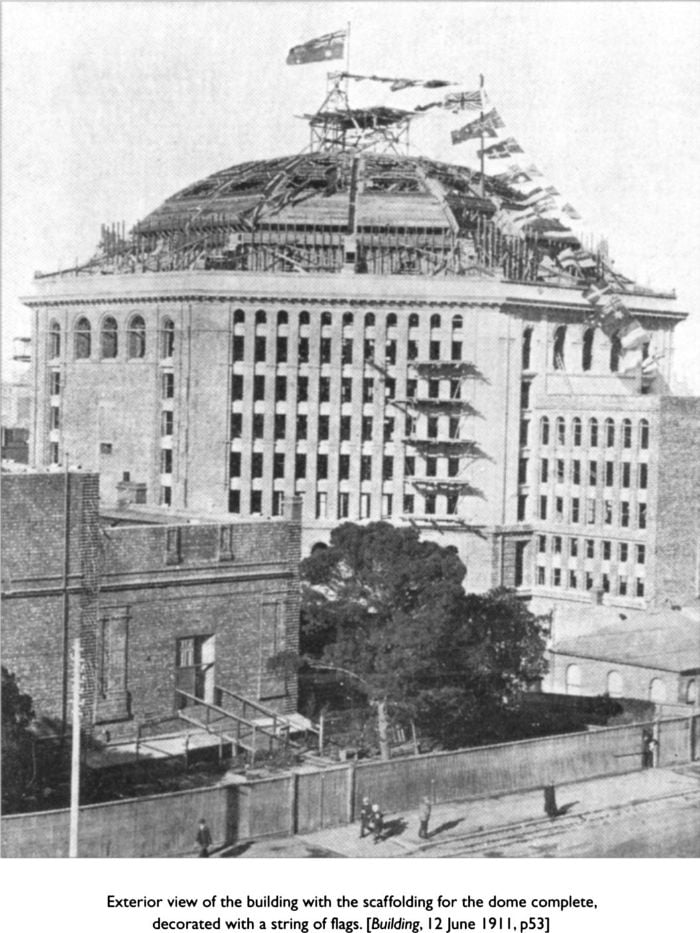Exterior view of the building with the scaffolding for the dome complete, decorated with a string of flags. [Building, 12 June 1911, p 53] [photograph]